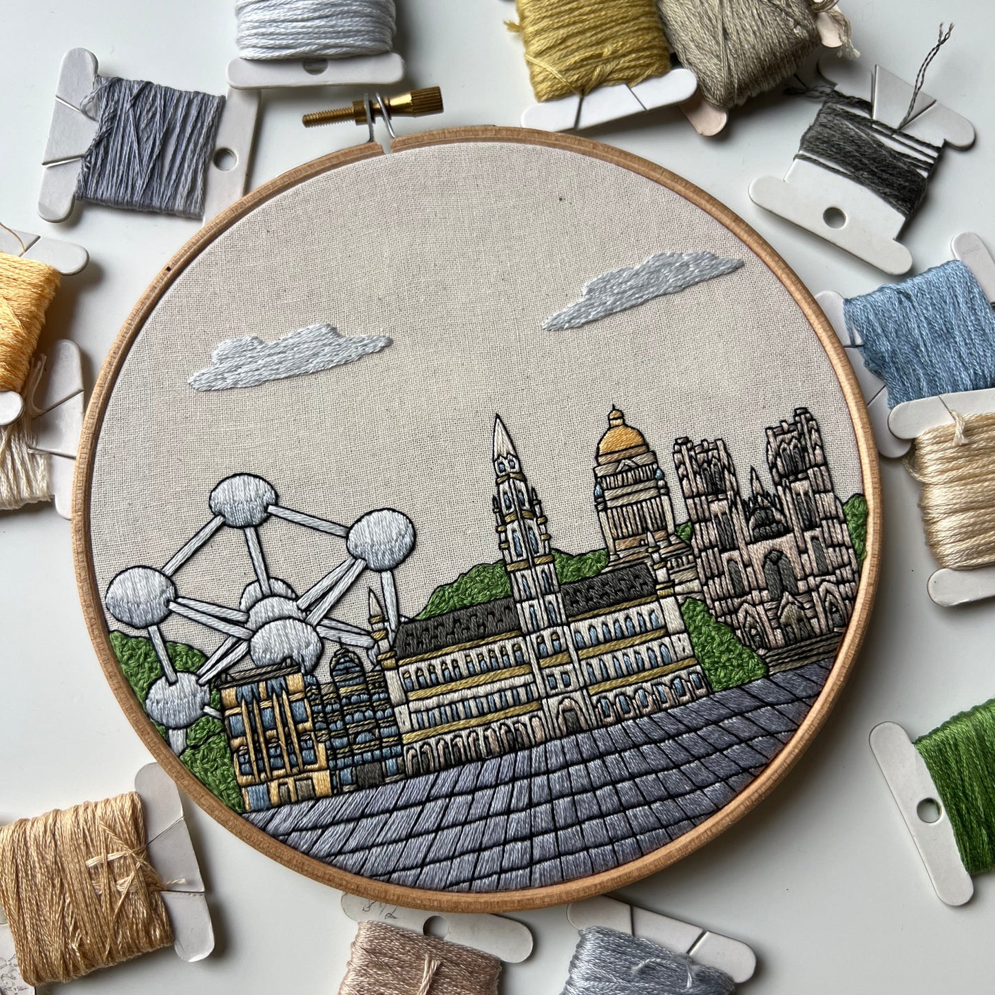Embroidery hoop with Brussels architectural design surrounded by bobbins of thread on a light background