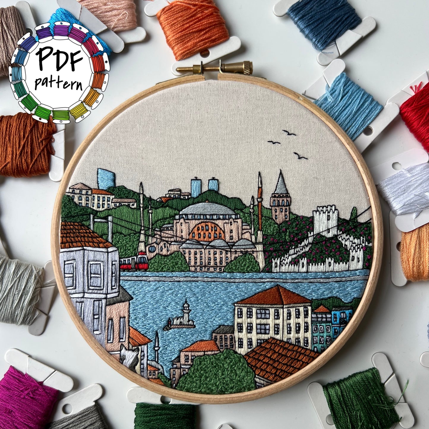Embroidery hoop with Istanbul cityscape design surrounded by bobbins of thread
