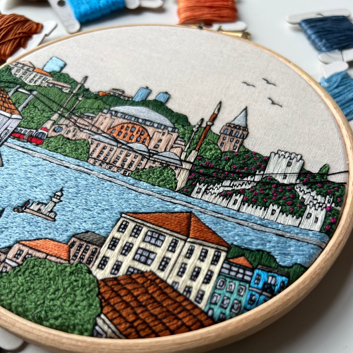 Embroidery hoop with a colorful cityscape design on a white background
