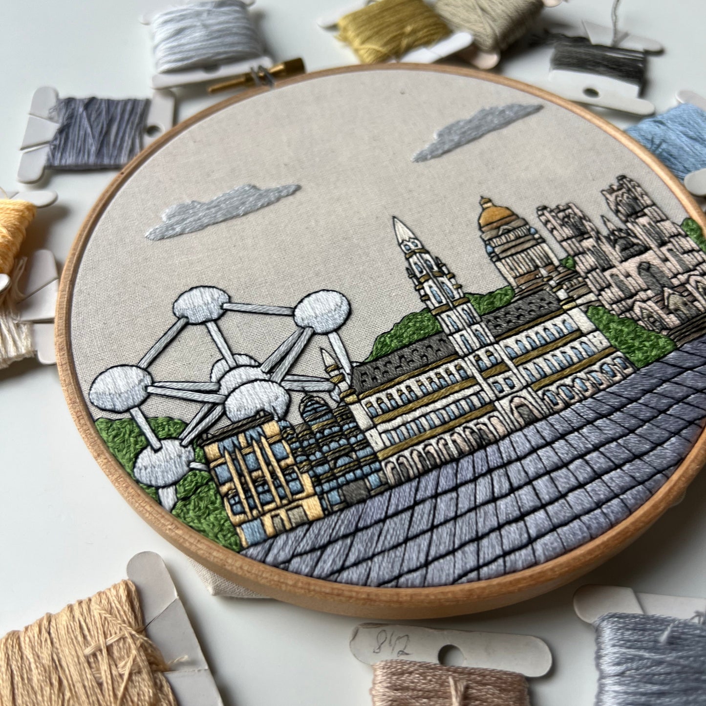 Embroidery hoop with Brussels architectural design surrounded by embroidery threads on a light background