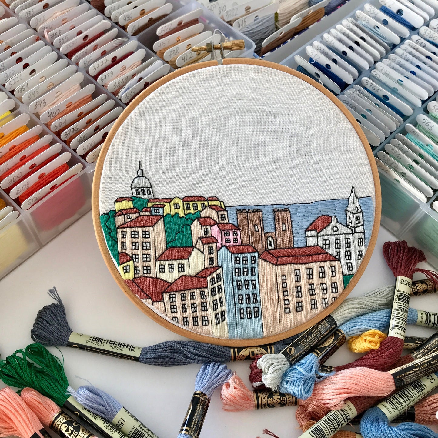 Embroidery hoop with a colorful cityscape design surrounded by embroidery threads.