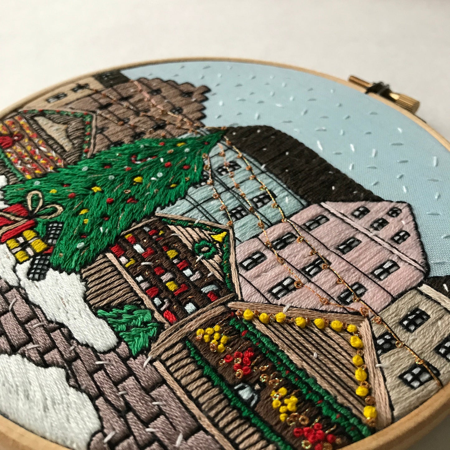 Embroidery hoop with a detailed embroidered scene of a village with houses and trees.