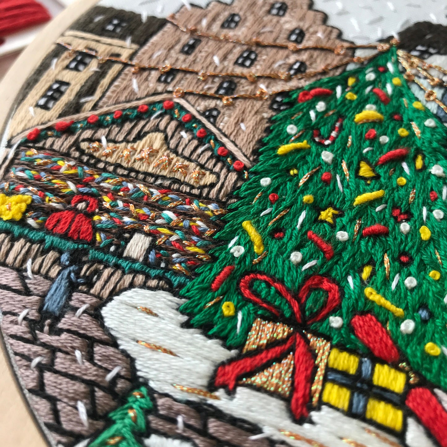 Embroidery hoop with a festive scene including a Christmas tree and houses.