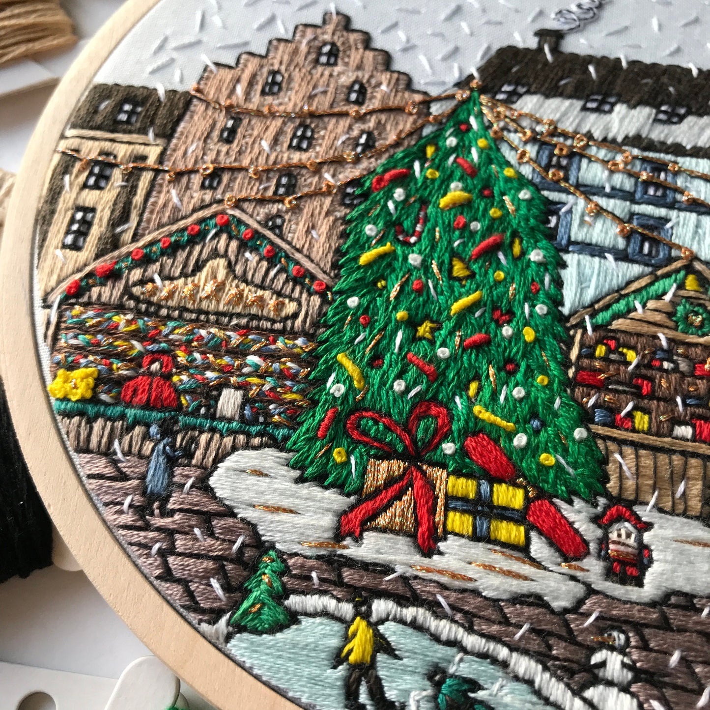 Embroidery hoop with a detailed Christmas scene including a tree, presents, and buildings.