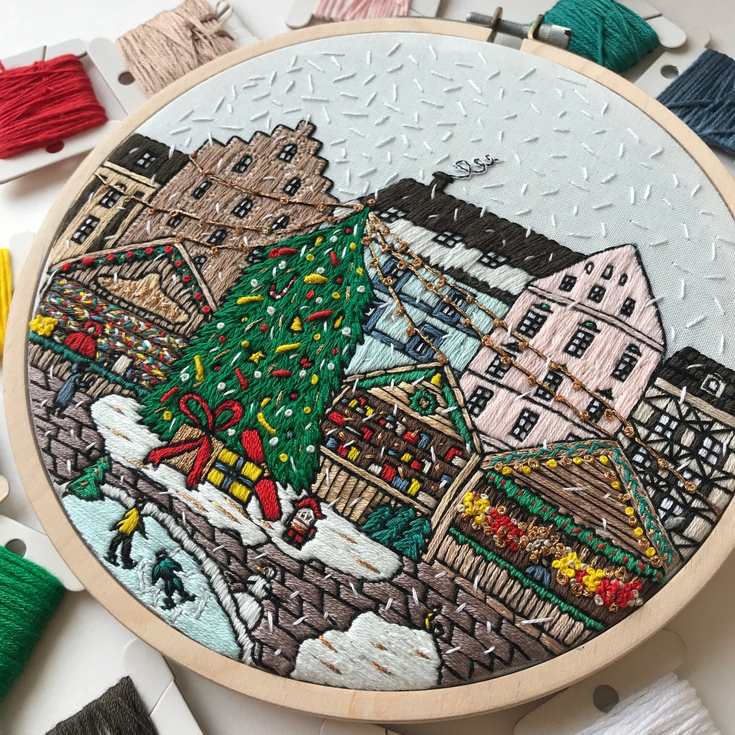 Embroidery hoop with a festive cityscape design featuring a Christmas tree and buildings.