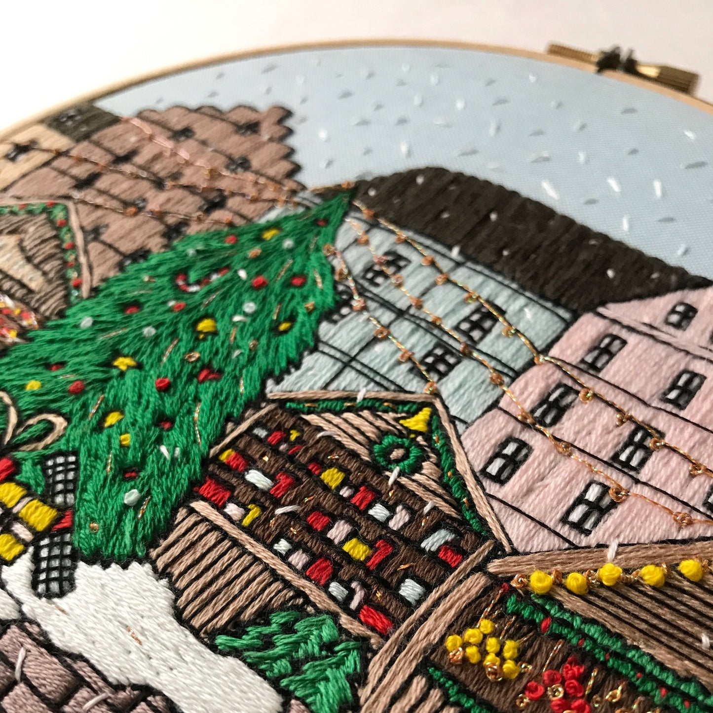 Embroidery hoop with a detailed landscape scene including houses, trees, and a windmill.