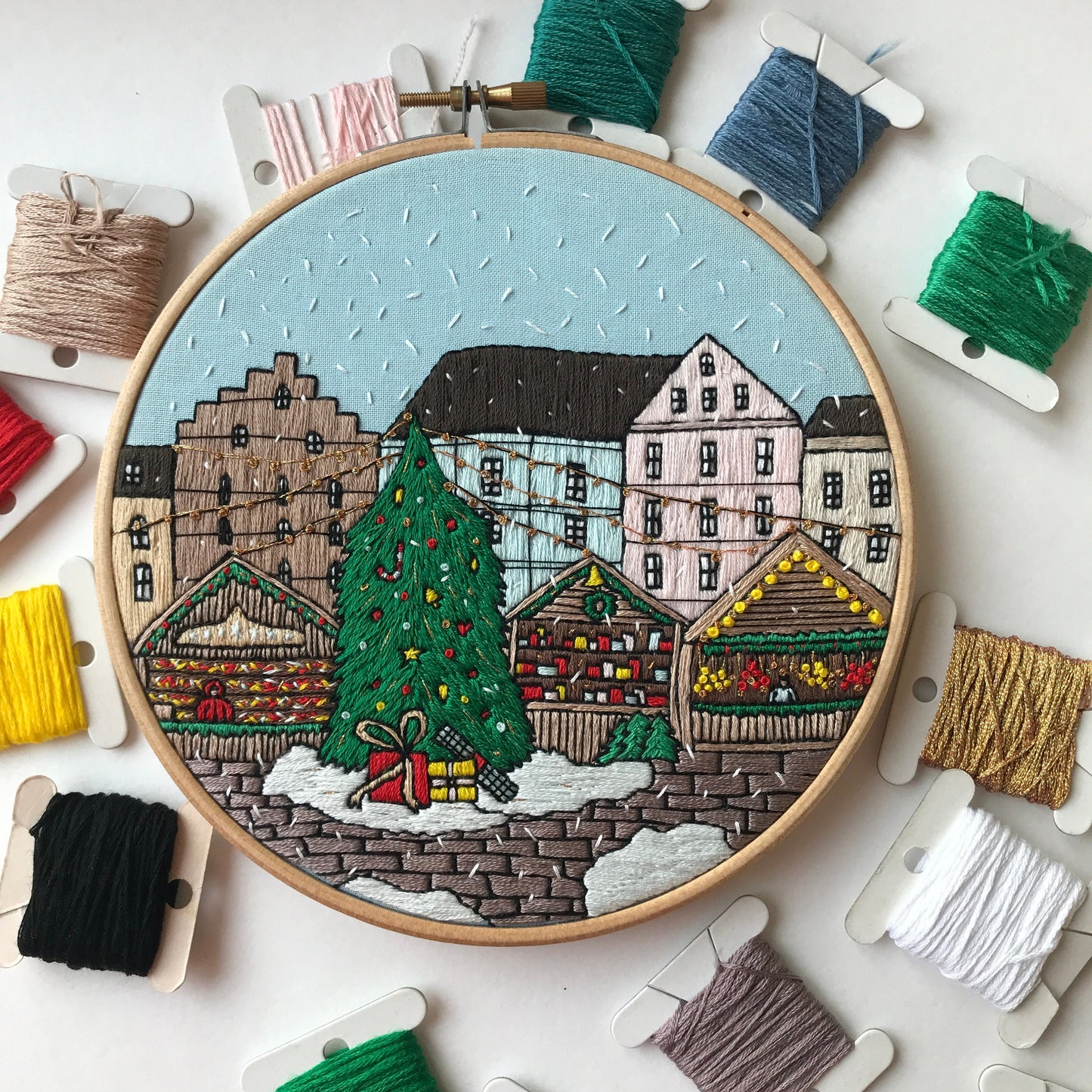 Embroidery hoop with a festive village scene surrounded by spools of thread.