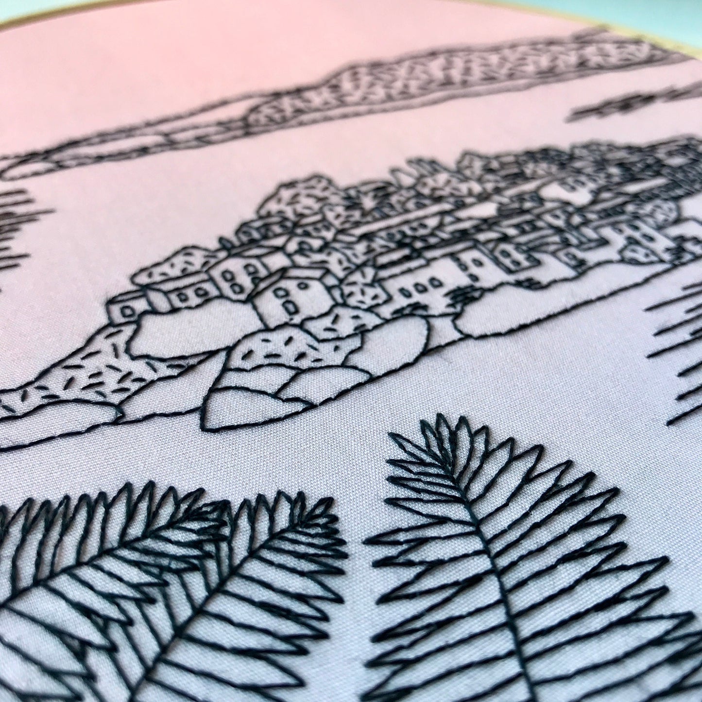 Embroidery of a coastal scene with houses and palm trees on fabric.