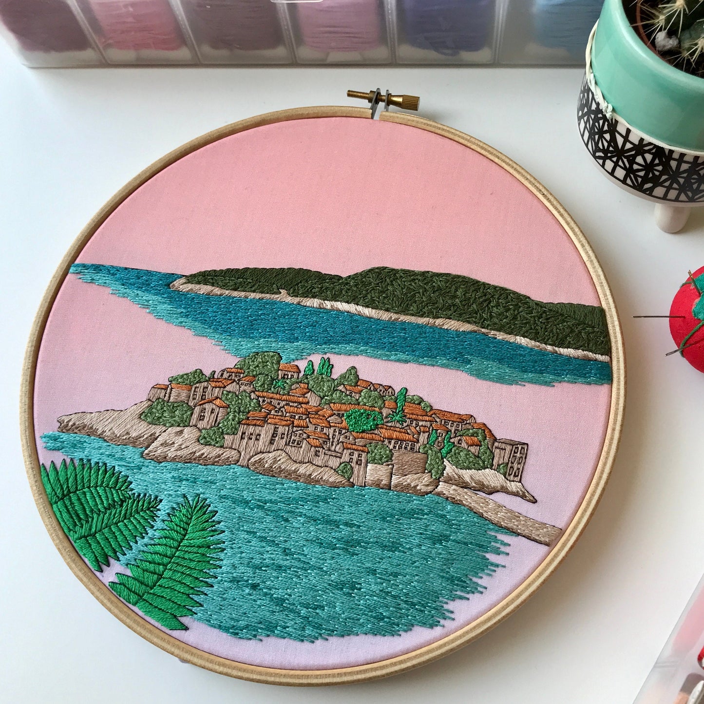 Embroidery hoop with a scenic landscape design on a pink background