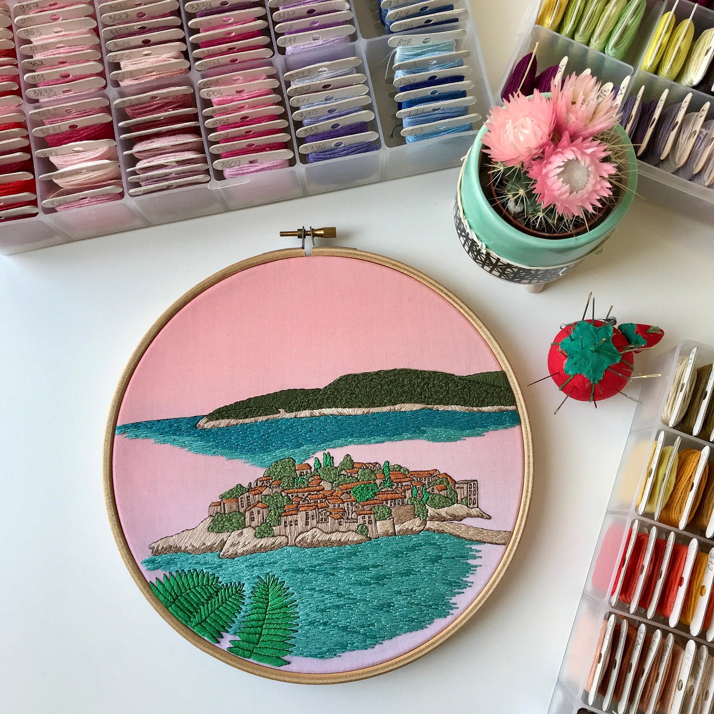 Embroidery hoop with a scenic landscape design on a table with embroidery supplies.