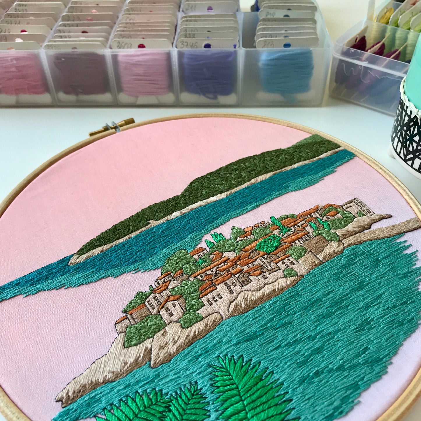 Embroidery hoop with a scenic landscape design on a pink background