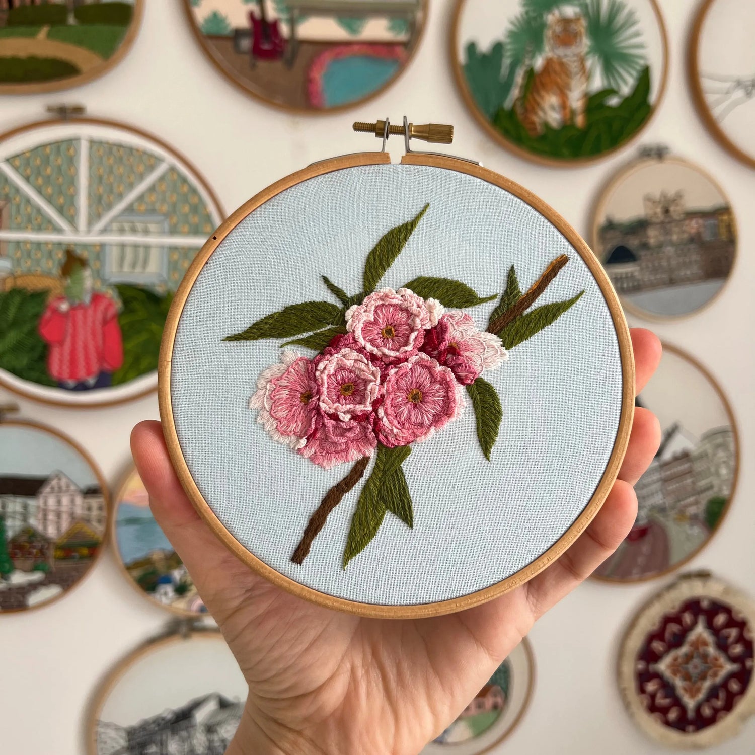 Delicate floral embroidery pattern with pink and green botanical motifs in wooden hoop