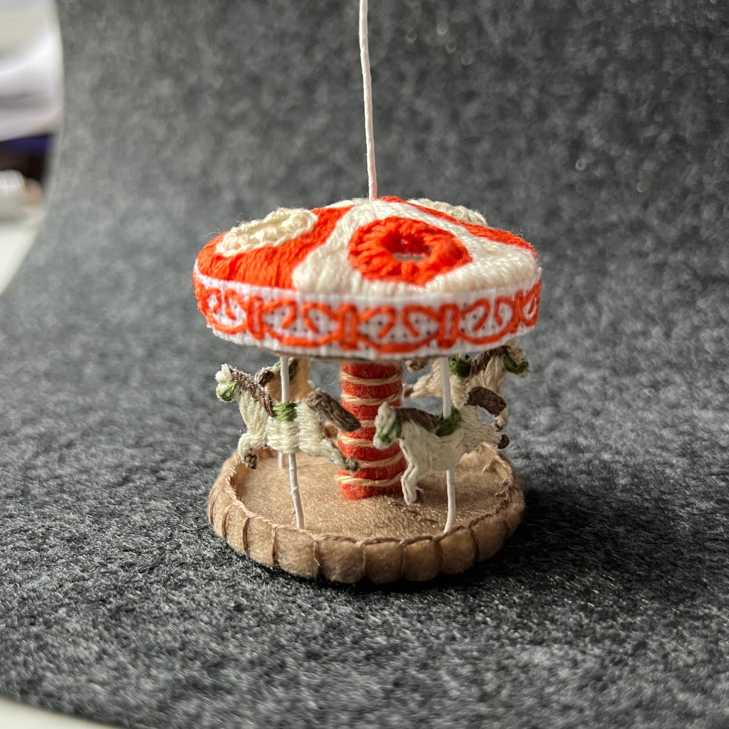 Small hand-embroidered carousel with horses on a gray surface