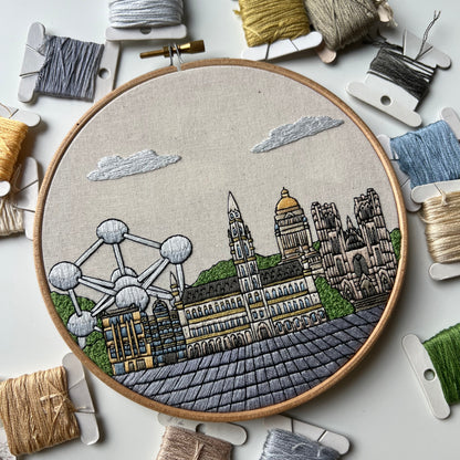 Embroidery hoop with  Brussels architectural design surrounded by bobbins of thread on a light background