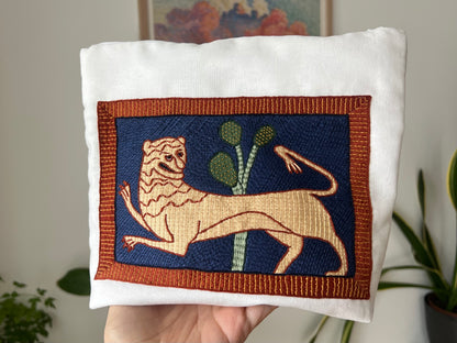 Embroidered lion design on a project bag with a blurred indoor background