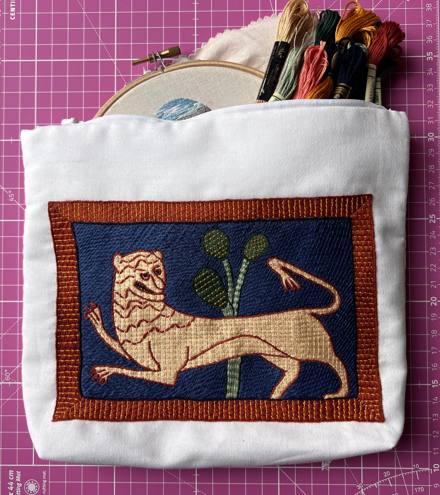 Embroidered pouch with a lion design on a pink grid background