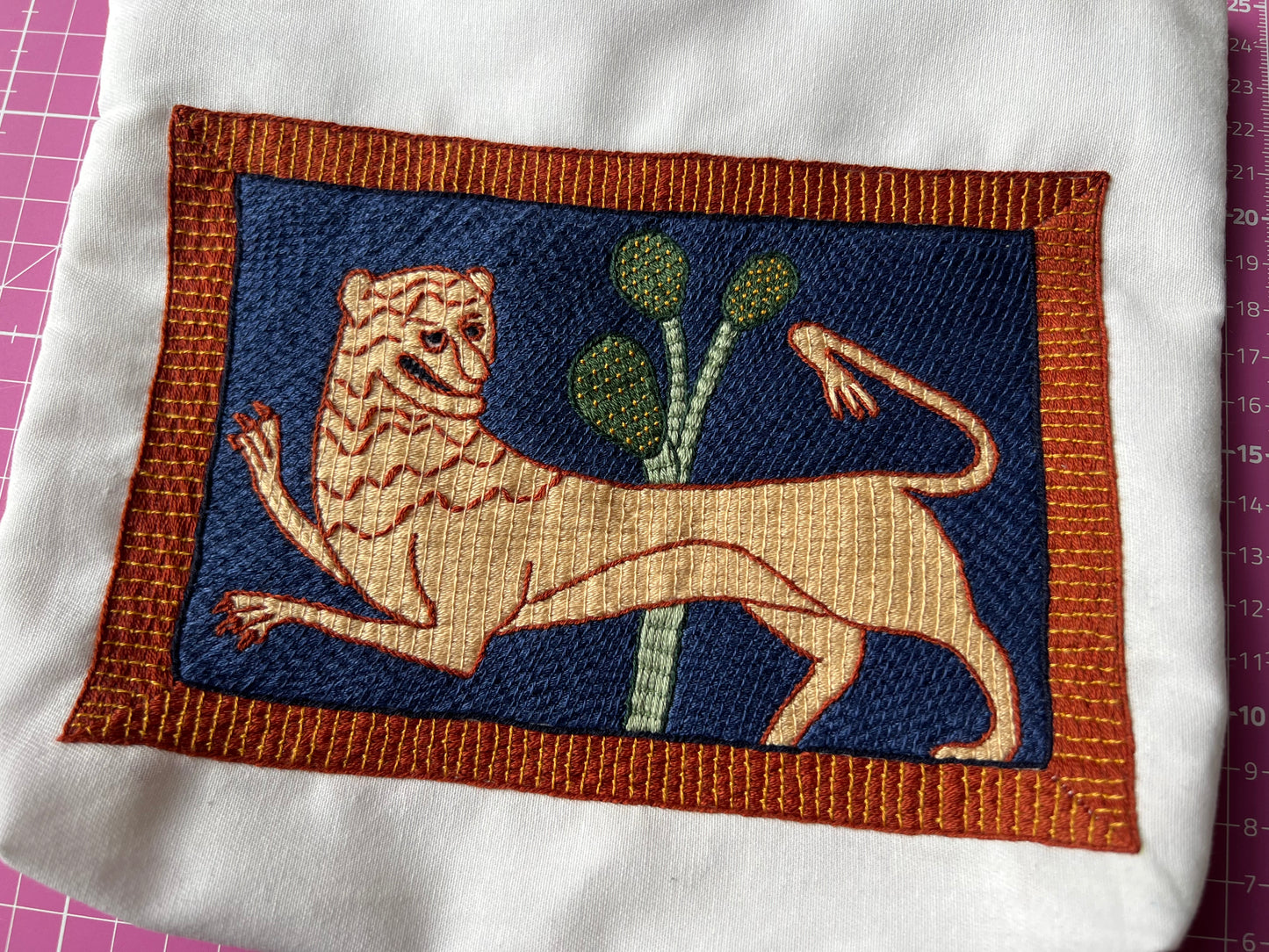 Embroidered patch of a lion and a plant on a blue background with brown border, on a white fabric.