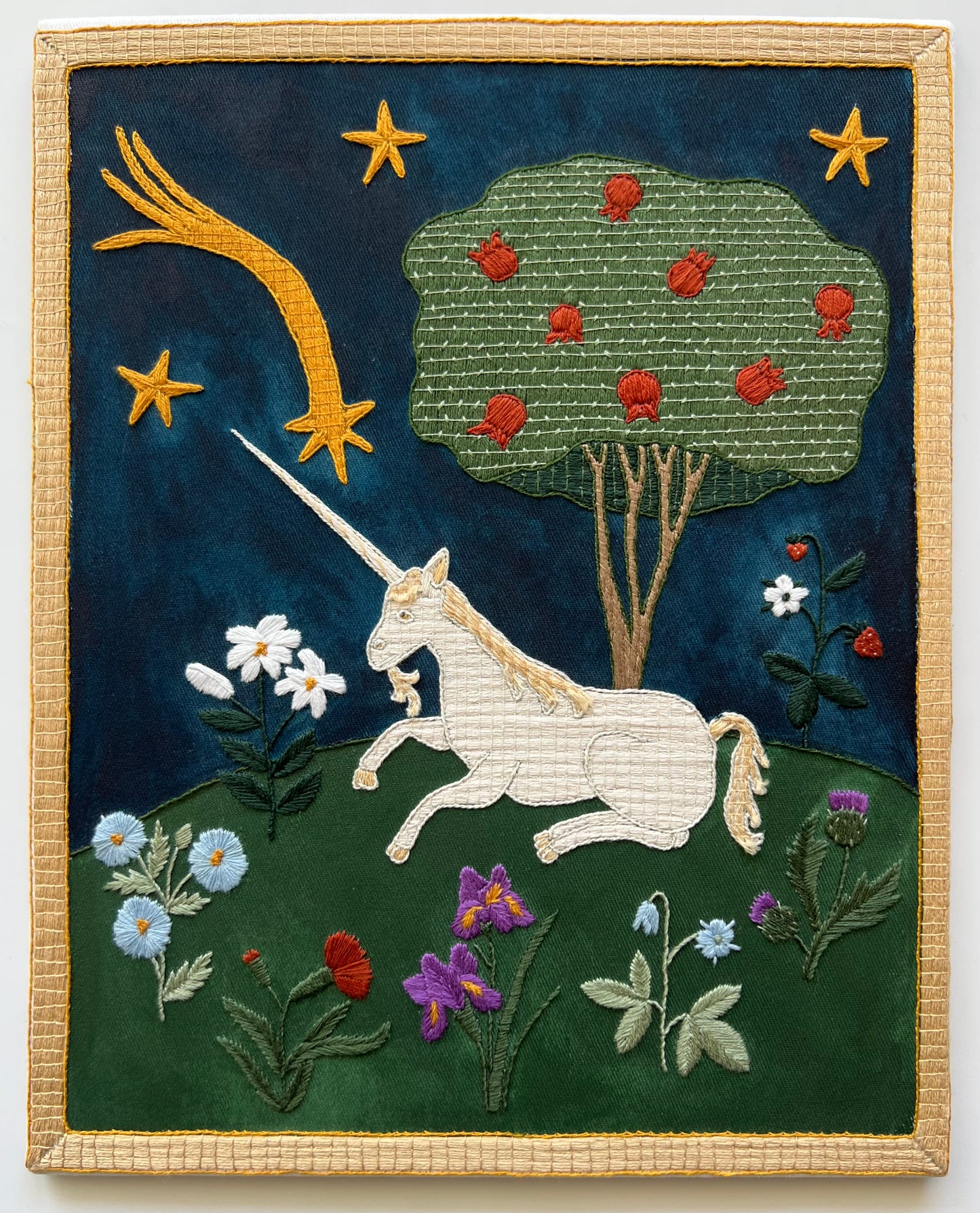 Embroidered artwork of a unicorn in a fantasy landscape with stars and flowers.