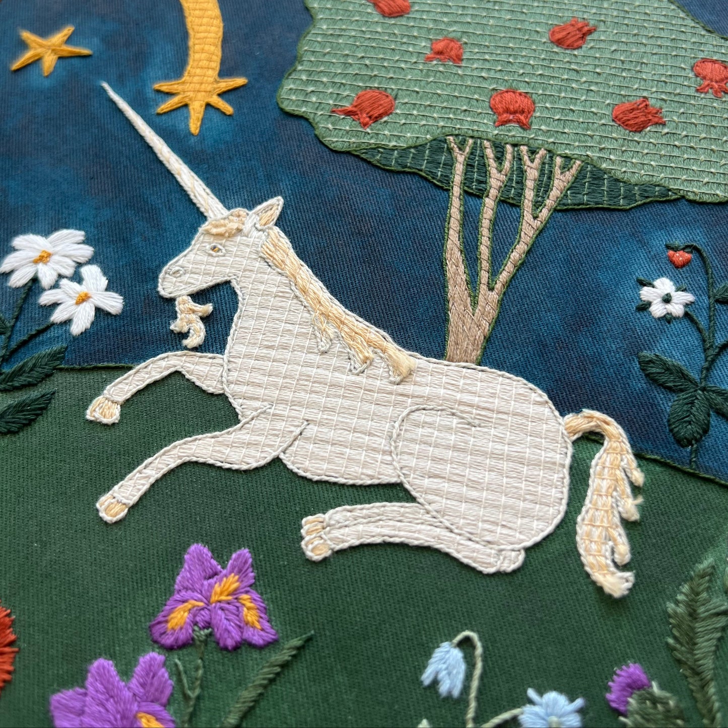 Embroidered panel with a unicorn, flowers, and trees on a dark blue background