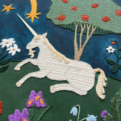 Embroidered panel with a unicorn, flowers, and trees on a dark blue background