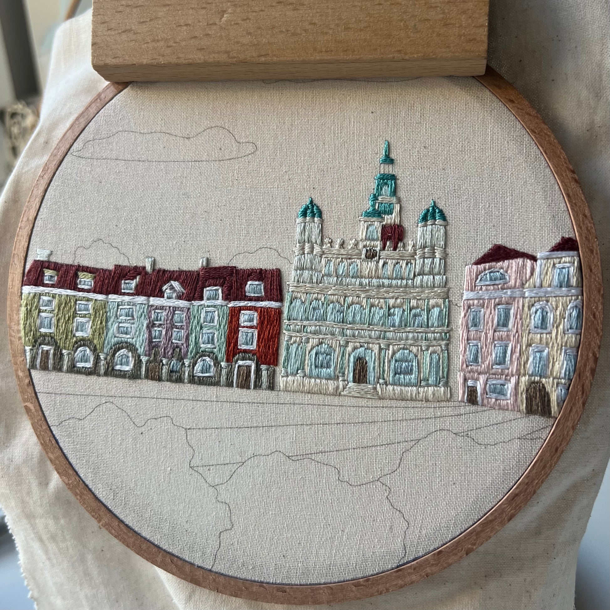 Embroidery of a cityscape with buildings in a wooden hoop, progress shot
