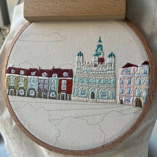 Embroidery of a cityscape with buildings in a wooden hoop, progress shot