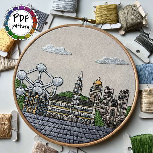 Embroidery hoop with a Brussels cityscape design surrounded by embroidery threads and tools.