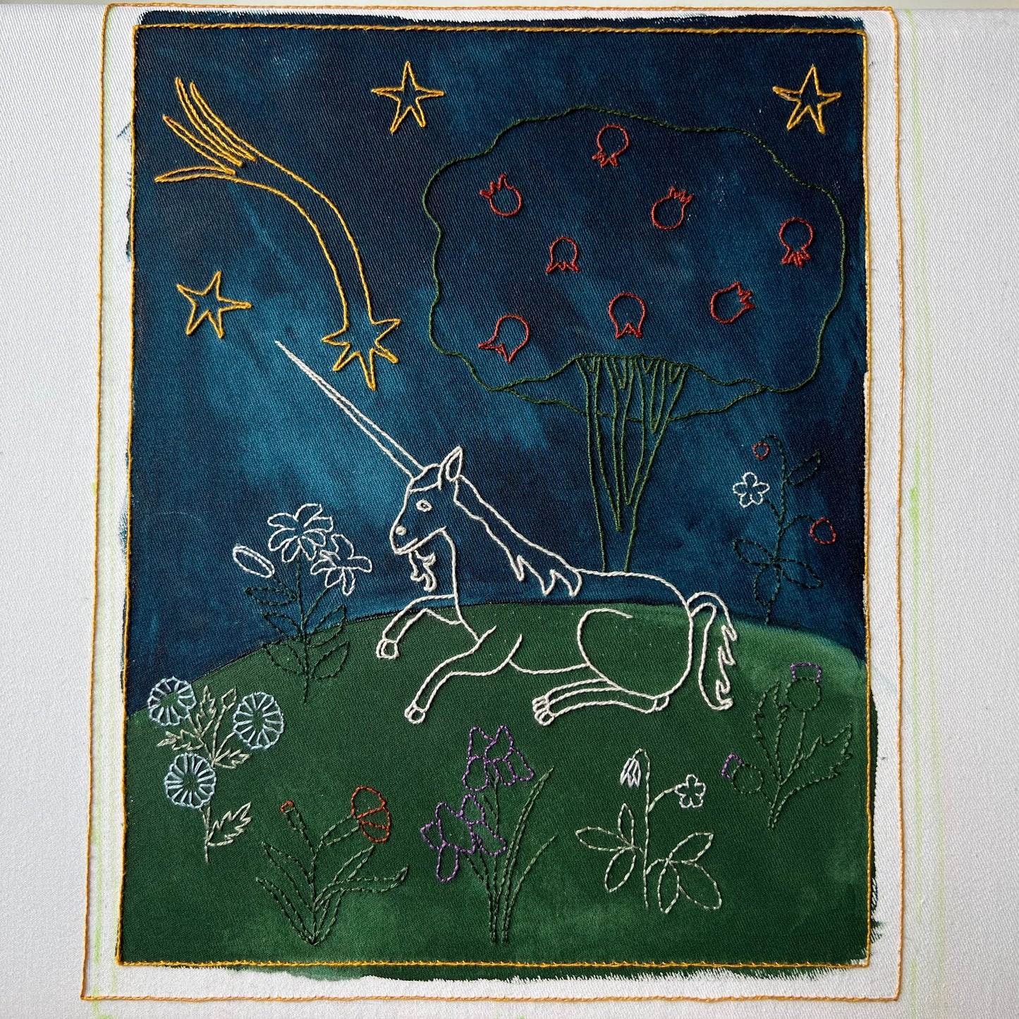 Embroidered artwork of a unicorn and celestial elements on a dark blue background.