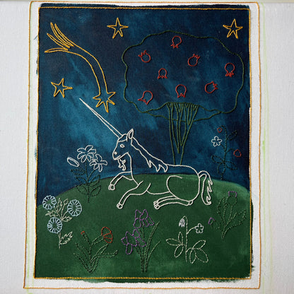 Embroidered artwork of a unicorn and celestial elements on a dark blue background.