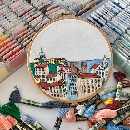 Embroidery hoop with a colorful cityscape design surrounded by embroidery threads.