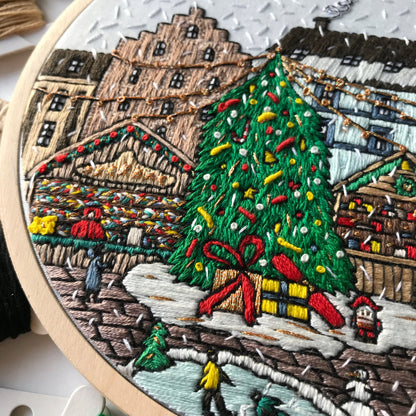 Embroidery hoop with a detailed Christmas scene including a tree, presents, and buildings.