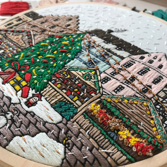 Embroidery hoop with a detailed embroidered scene of a Christmas village.