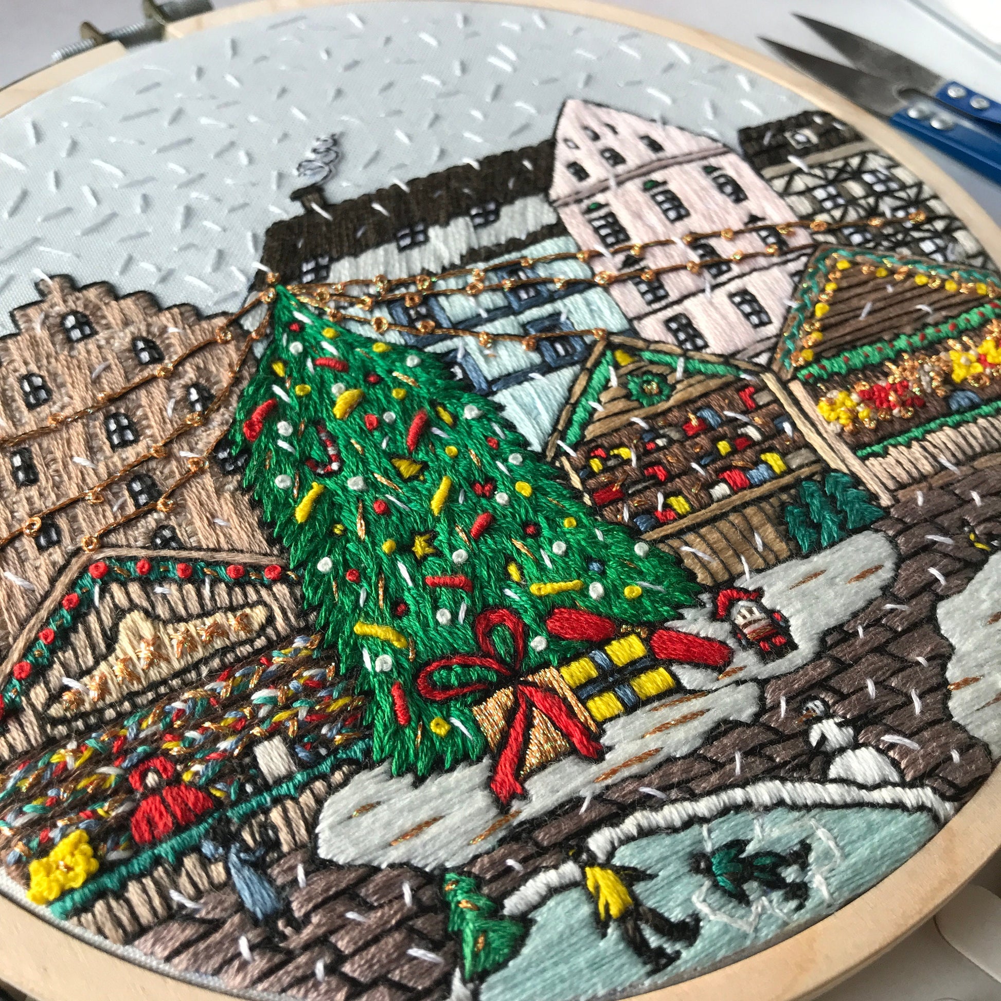 Embroidery of a festive scene with a Christmas tree and buildings in an embroidery hoop.
