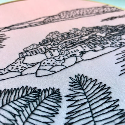Embroidery of a coastal scene with houses and palm trees on fabric.