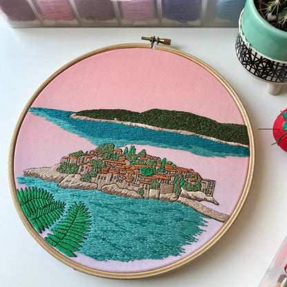 Embroidery hoop with a scenic landscape design on a pink background