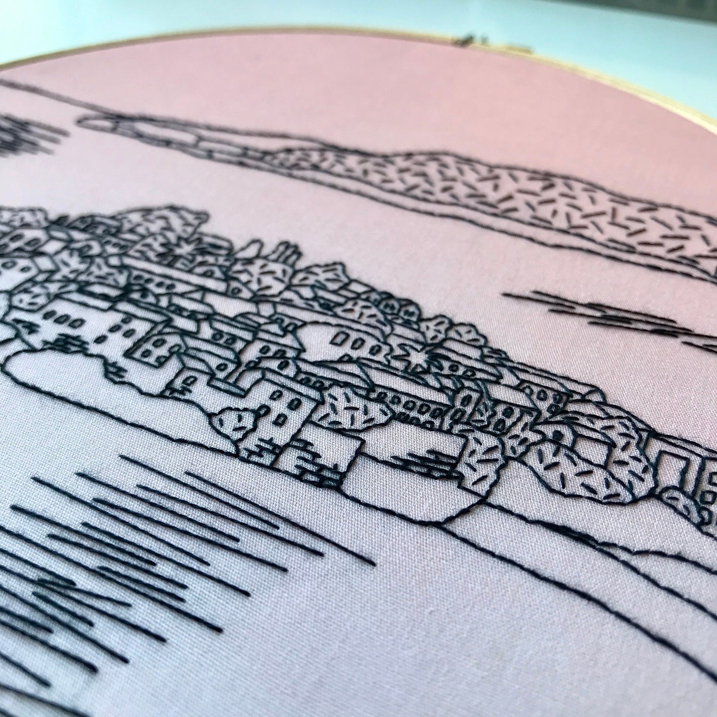 Embroidery of a coastal town with mountains in the background