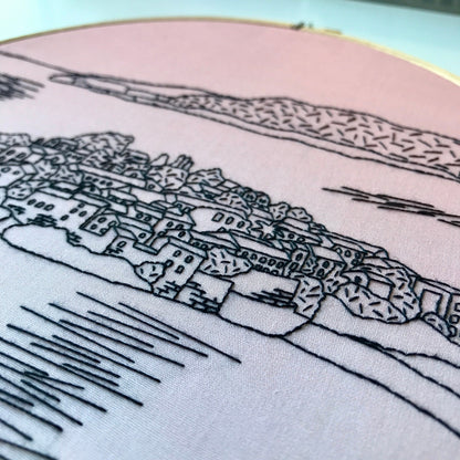 Embroidery of a coastal town with mountains in the background