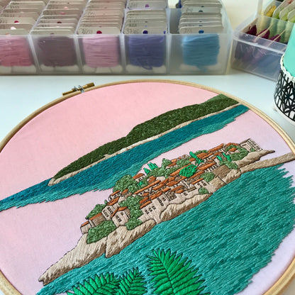 Embroidery hoop with a scenic landscape design on a pink background